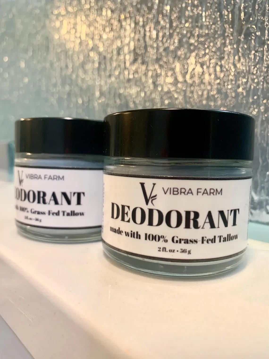 Image of Blue Tansy Grass Fed Tallow Deodorant in a beautiful bathroom on a white marble shelf with another container slightly blurred in the background.