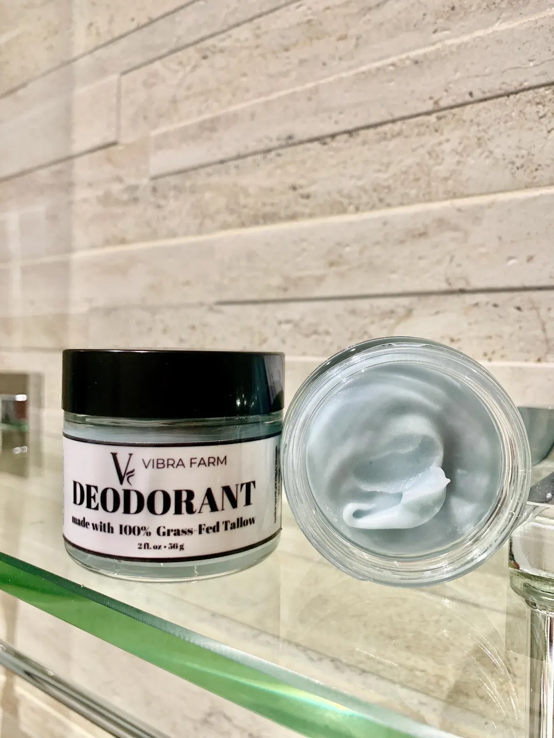 Image of Blue Tansy Grass Fed Tallow Deodorant in a beautiful bathroom on a glass shelf with the container open showing the beautiful blue tansy color in the tallow.