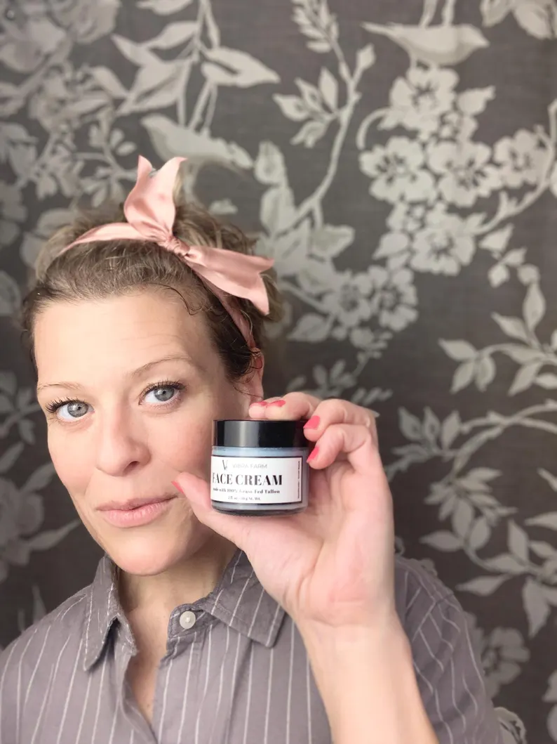 Image shows the Blue Tansy Oil, Honey, Jojoba and Vitamin E Whipped Tallow Face Cream from Vibra Farm with Lindsay holding up a close container of the cream.