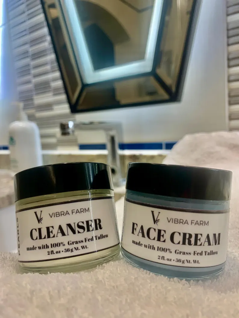 Image shows the Blue Tansy Oil, Honey, Jojoba and Vitamin E Whipped Tallow Face Cream from Vibra Farm with a container of the Vibra Farm Cleanser on a stunning bathroom sink.